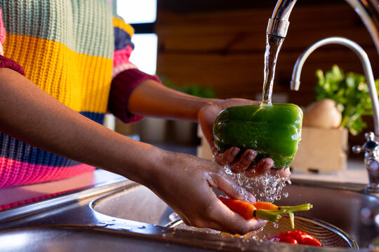 Midsection of african american woman preparing meal washing vegetables at sink in sunny kitchen