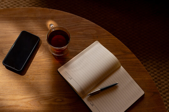 Notebook, tea and smartphone on table with sunlight, copy space