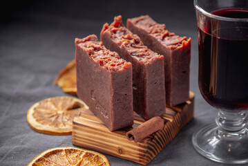 Pieces of natural soap on a wooden soap dish, a glass of mulled wine, slices of orange and cinnamon stick. Festive and cozy atmosphere, organic handmade soap
