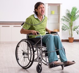 Young male invalid in wheel-chair suffering at home