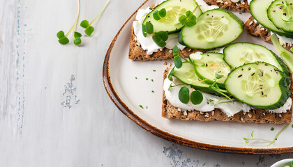 Breakfast, cereal bread sandwiches, cream cheese, sliced cucumber, with micro greenery on a light table, close-up, top view, selective focus, no people,