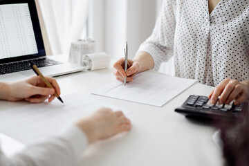 Two accountants using a calculator and laptop computer for counting taxes at white desk in office. Teamwork in business audit and finance