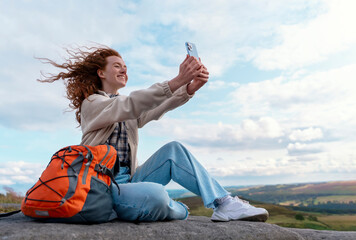 woman traveler in a white  jacket and orange backpack traveling mountains and taking photos by...