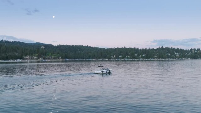 Drone flying over speedboat moving on Lake Arrowhead in the San Bernardino Mountains, Los Angeles, California, USA. Motorboat driving along the lakeshore in evening. Summer water sports, 4k footage