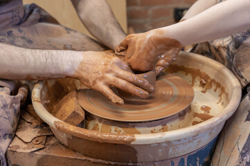 potter teaches the child. A craftsman sits on a bench with a potter's wheel and makes a clay pot. National craft. Hands close-up