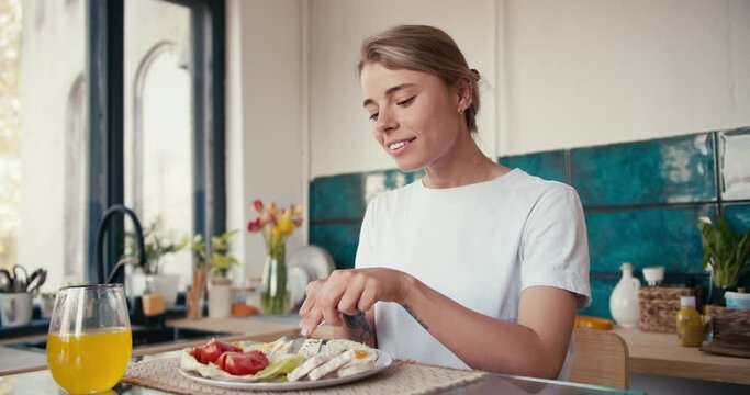 Blonde girl in a white T-shirt trying breakfast in the sunny kitchen on a spring morning
