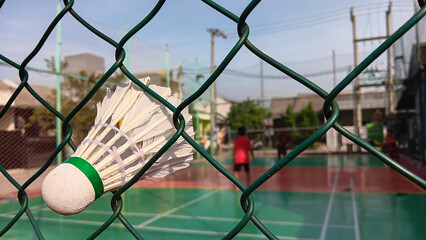 Fototapeta na wymiar Shuttle cock badminton stuck in the fence net with the players in the background