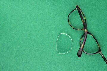 Old broken eyeglasses with damaged lens on green background. Poor eyesight. Reuse and repair...
