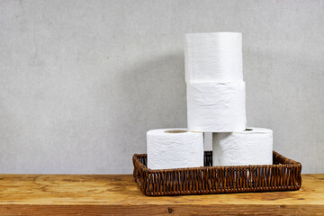 whicker basket with rolls of toilet paper on wooden board table with copy space 