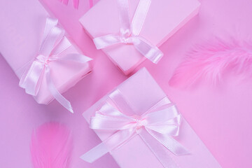 pink gift boxes with pink bows on a pink background decorated with feathers, top view, the concept of celebrating a girl's birthday, party, anniversary in pink colors, or sale and shopping or a