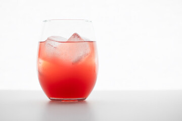 Close frontal view of a red cocktail drink with ice cubes in a glass on white background with copt space