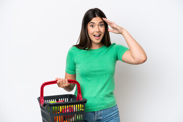 Young Brazilian woman holding a shopping basket full of food isolated on white background with surprise expression
