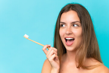 Young caucasian woman isolated on blue background with a toothbrush and surprised expression