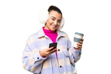Young woman wearing winter muffs over isolated chroma key background holding coffee to take away...