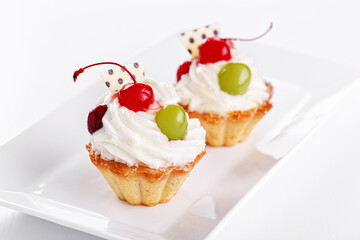 Beautiful cream cakes with cherries and grapes on a plate on a white background