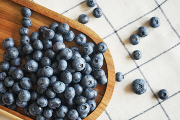 Blueberries lie in a wooden dish on a checkered tablecloth  