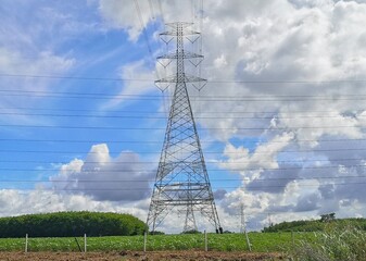 High voltage pole, located in the middle of a green meadow, with a blue sky and white clouds in the...