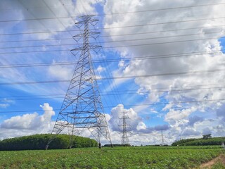 High voltage pole, located in the middle of a green meadow, with a blue sky and white clouds in the...