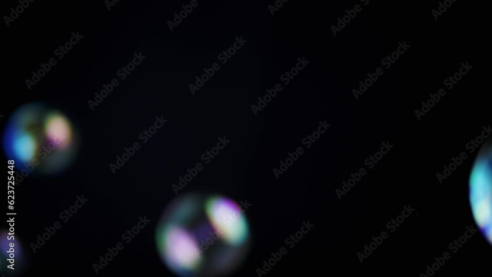 Poster colorful soap bubbles fly in an empty space on isolated black background. many large, small rainbow 