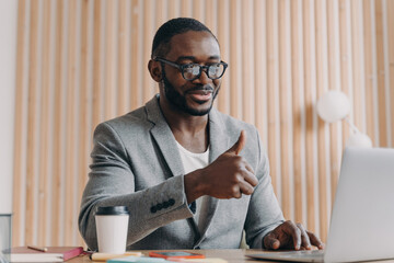 Happy African American employee in glasses, online conversation with client/partner, thumbs up, smiling, cheerful businessman, video call at work.