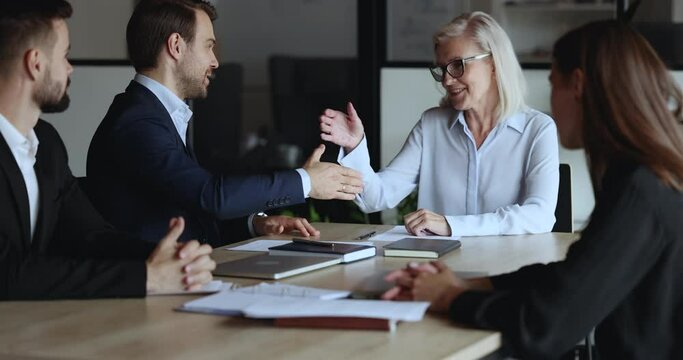 Positive business professional man thanking mature senior partner, colleague, mentor woman for help, training seminar, good job, giving feedback, shaking hand on corporate meeting