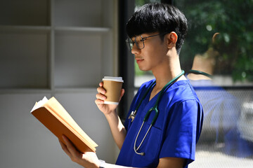 Medical student man wearing blue scrubs reading book, preparing for university exams. Medical...