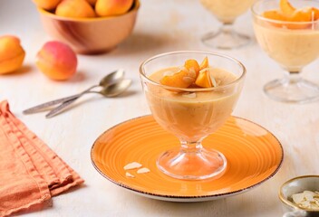 Dessert, mousse or panna cotta with apricots and almond petals in transparent bowls on a light...