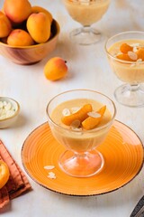 Dessert, mousse or panna cotta with apricots and almond petals in transparent bowls on a light concrete background. Summer desserts, fruit mousses and jellies.