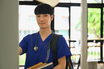 Photo of medical student standing at lockers in campus and smiling to camera. Medical internship...