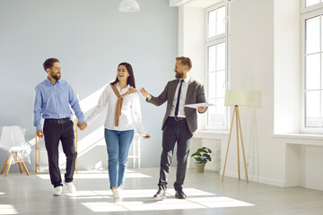 Fototapeta premium Real estate agent conducts tour for prospective tenants or potential home buyers. Happy man and woman are enthusiastically looking at house, holding hands and consulting with real estate expert.