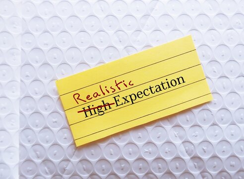 Note on envelope with handwritten text HIGH EXPECTATION crossed HIGH of fto REALISTIC, means  to be able to move forward in life with more acceptance when things turn out lower than expected