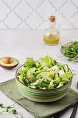 Healthy food, green salad with avocado, cucumber, microgreens and feta cheese in a green salad bowl on a light concrete background. Green monotone.