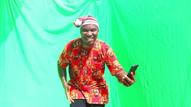 Happy man dance back and forth to good news on his phone of a good business deal concluded bending and shaking hips in cultural African dance