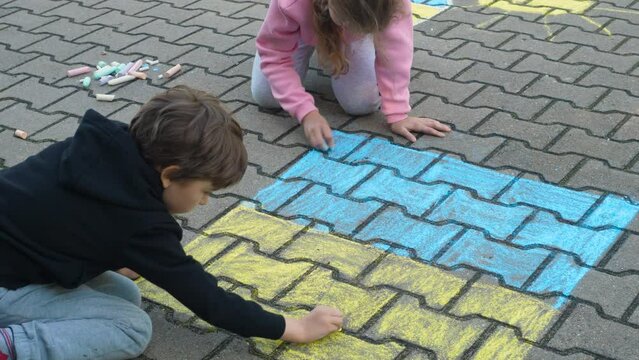 Children Draws With Chalk on Pavement Drawing of Big Ukrainian Flag. Little Girl and Boy Drawing Ukrainian Flag With Chalk. Crisis, Peace, Stop Aggression, Children Against War. Freedom to Ukraine.