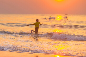 A young Fisherman throwing a net to the sea at sunrise in Thailand.
