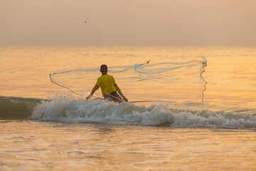 A young Fisherman throwing a net to the sea at sunrise in Thailand.