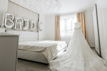 chic white wedding dress with a long train in the bedroom of the bride