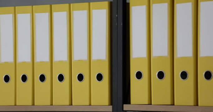 Mockup with a white label on the spine of yellow folders with office documents standing on a wooden shelf in row. Storage of business documents