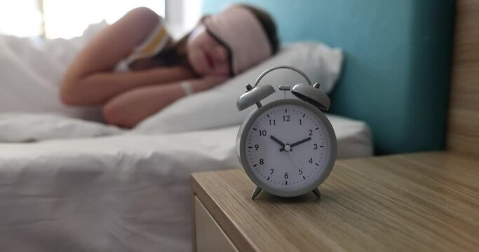 Alarm clock for 10 o'clock on table in children bedroom. Child teenager sleeping in sleep mask