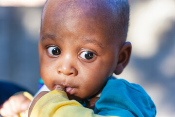 african baby outdoors with his thumb in the mouth
