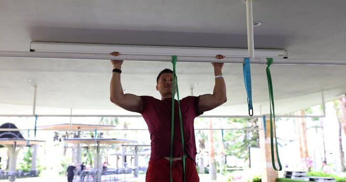 Young man pulls up on horizontal bar with elastic band outdoors. Concept of fitness sport exercise training and lifestyle