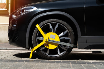 Car wheel blocked by a yellow metal lock or clamp. Vehicle illegal parking violation in a...