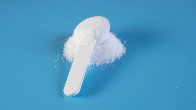 Pile of Aspartame powder with measuring spoon on blue background. Video 4K, Rotating. Sugar substitute, artificial sweetener. Food additive E951 used as sugar substitute in foods and beverages.