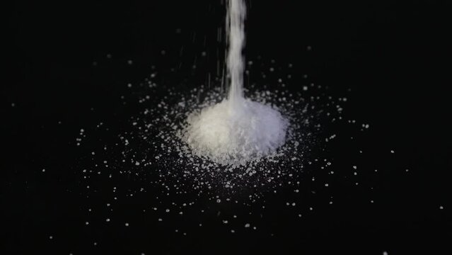 Aspartame powder falls on black surface. Food additive E951. Aspartame is an artificial non-saccharide sweetener 200 times sweeter than sucrose, used as sugar substitute in foods and beverages.