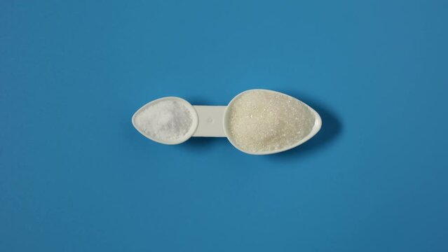 Sugar and Aspartame sweetener in measuring spoon, top view. Video 4K, Rotating. Sugar substitute, artificial sweetener. Food additive E951 used as sugar substitute in foods and beverages.