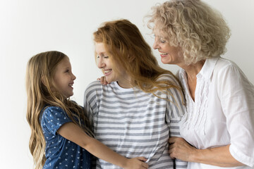 Cheerful girls and women of three female generations standing close at white wall background, hugging, talking, laughing, enjoying bonding, leisure, relationships. Family portrait