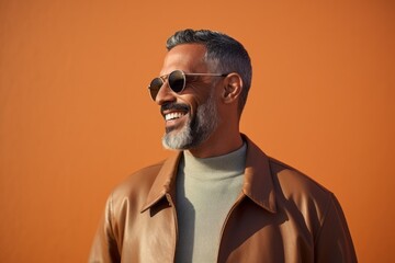 Fototapeta premium Portrait of a handsome mature man in sunglasses and brown coat on an orange background