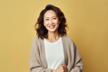 Fototapeta premium Portrait of a smiling asian woman looking at camera over yellow background