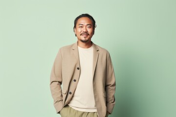 Fototapeta premium Young asian man in beige jacket and green trousers on light green background
