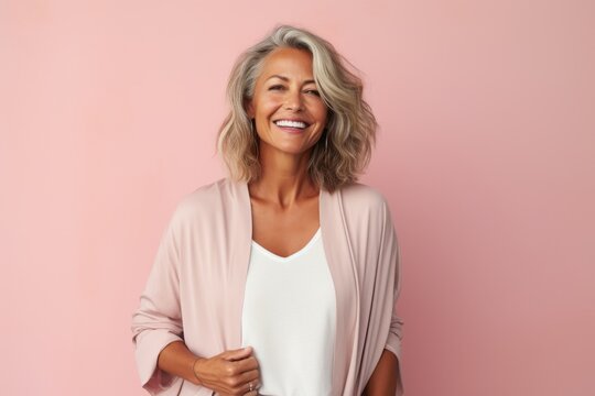 Portrait of a happy mature woman smiling at camera against pink background